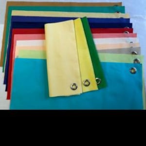 May include: Assortment of fabric swatches in various colours, including teal, yellow, green, red, pink, beige, and blue. The swatches are laid out in rows on a flat surface. Some swatches have metal eyelets.
