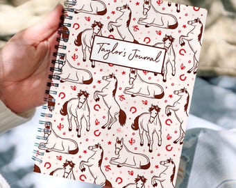 May include: A spiral-bound journal with a cream-colored cover featuring a repeating pattern of brown horses, red horseshoes, and stars. The journal has the text "Taylor's Journal" in a rectangular box.