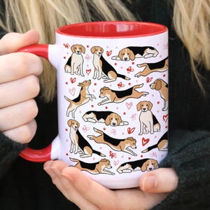 Könnte beinhalten: Weiße Keramiktasse mit rotem Rand und Henkel. Die Tasse zeigt ein sich wiederholendes Muster von Beagle-Hunden in verschiedenen Posen, mit rosa Herzen und Blumen.
