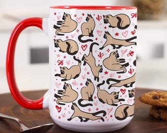 May include: White ceramic coffee mug with a red rim and handle. The mug features a repeating pattern of Siamese cats with pink hearts and stars on a white background.