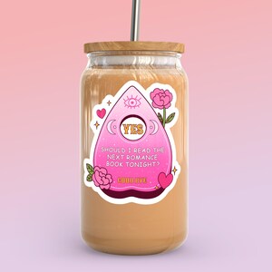 Op de afbeelding: Een roze en witte sticker met een Ouija-bordontwerp op een glazen pot met een bruin deksel. De sticker zegt "JA" en "Moet ik vanavond het volgende romanboek lezen? Tot ziens".