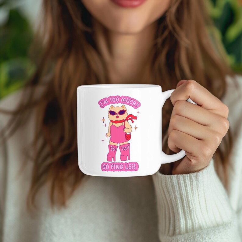 Puede incluir: Taza de cer&aacute;mica blanca con un gato de dibujos animados rosa que lleva gafas de sol y un vestido rosa. La taza tiene el texto "I'm too much? Go find less." impreso en ella.