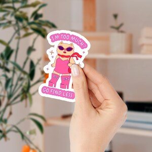 Puede incluir: Una pegatina rosa y blanca con un perro de dibujos animados que lleva gafas de sol y un vestido rosa. El texto de la pegatina dice "&iquest;Soy demasiado? Ve a buscar menos."