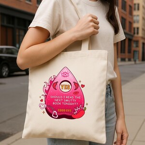 Op de afbeelding: Een witte tote bag met een roze en rode afbeelding van een Ouija-bord met de tekst "YES" en "SHOULD I READ THE NEXT SMUTTY BOOK TONIGHT? GOOD BYE".