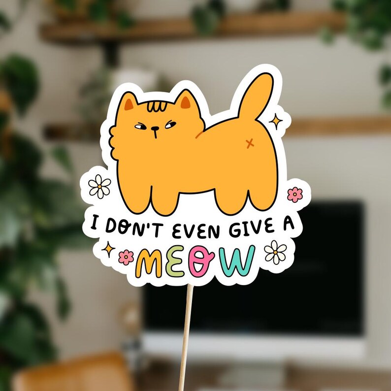 以下が含まれることがあります： 不機嫌そうな表情をしたオレンジ色の漫画の猫が描かれた白いステッカー。猫は視聴者に向かって背中を向けて座っています。猫の下には「ニャーも言わない」というカラフルな文字が書かれています。