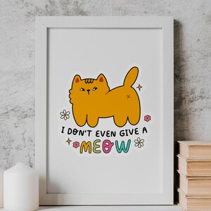 以下が含まれることがあります： 白い額縁に入ったプリント。オレンジ色の漫画の猫が「ニャーも言わない」という文字をカラフルな文字で書いている。