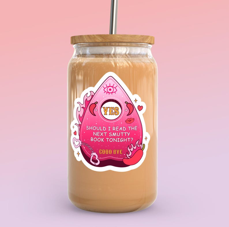 May include: A glass tumbler with a wooden lid and a metal straw. The tumbler has a sticker with a pink Ouija board design, flames, and the text "SHOULD I READ THE NEXT SMUTTY BOOK TONIGHT? GOOD BYE."