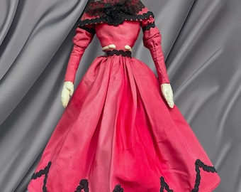 Puede incluir: Muñeca antigua de porcelana con cabello negro, vestida con un vestido rosa con ribetes de encaje negro y un chal de encaje negro.