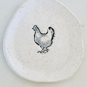 May include: White ceramic dish with a speckled finish and a black and white silhouette of a chicken in the center.