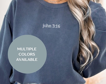 Può includere: Una felpa blu-grigio con la scritta "john 3:16" stampata sul davanti. Un grafico circolare con la scritta "MULTIPLE COLORS AVAILABLE" si trova in basso a sinistra. La felpa ha un girocollo e maniche lunghe.