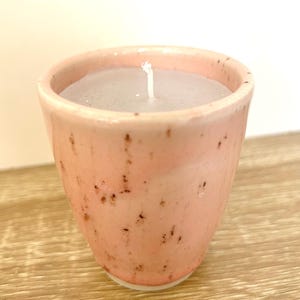 Op de afbeelding: Een kleine, roze keramische kaars in een gespikkelde beker. De kaarswas is lichtgrijs van kleur en een witte lont is gecentreerd in de beker. De beker heeft een licht uitlopende vorm en een gladde, glanzende afwerking. Woondecoratie-artikel.
