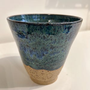 May include: A ceramic cup with a blue and green glaze. The cup has a brown rim and a speckled texture.