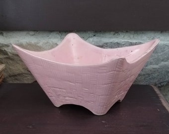 May include: A pink ceramic bowl with a woven pattern. The bowl has a unique, angular shape with four legs.