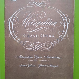 May include: A vintage program cover for the Metropolitan Grand Opera, with white script on a brown background. The cover includes the text "1947 - Twenty-Second Season - 1947" and the dates "April 7-12" for the Cleveland Public Auditorium.