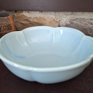 May include: A light blue ceramic bowl with a scalloped edge. The bowl has a smooth, glossy finish and a shallow design. The bowl is likely vintage and is suitable for serving or display.