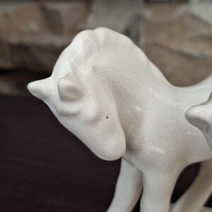 Pode incluir: Um close-up de uma estatueta de cavalo de cer&acirc;mica branca. O cavalo est&aacute; em p&eacute; com a cabe&ccedil;a ligeiramente virada. A cer&acirc;mica tem um acabamento craquelado e os detalhes das caracter&iacute;sticas do cavalo s&atilde;o vis&iacute;veis.