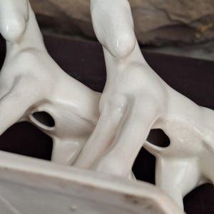 Pode incluir: Estatueta de cavalo de cer&acirc;mica creme com dois cavalos voltados para a mesma dire&ccedil;&atilde;o. Os cavalos t&ecirc;m um design elegante e minimalista com pesco&ccedil;os alongados e orelhas pequenas. A estatueta tem uma base retangular.
