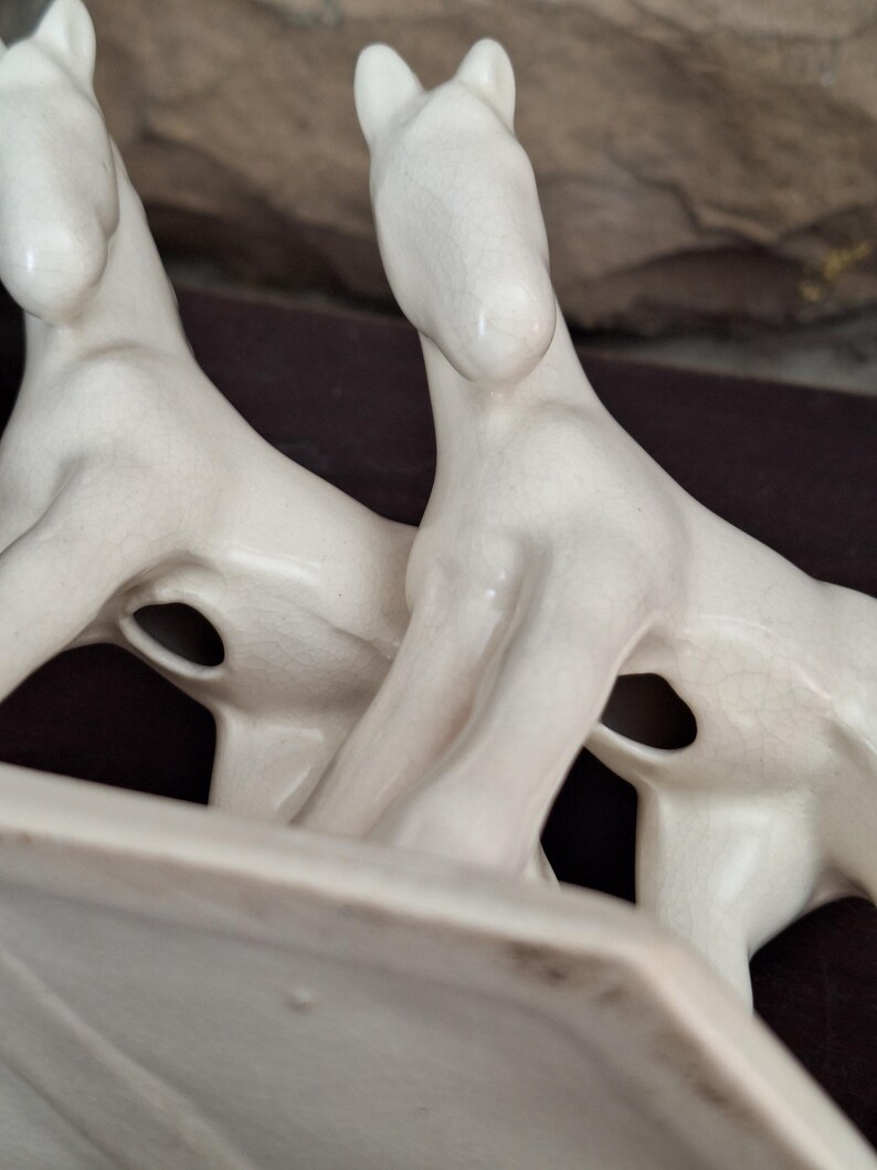 Pode incluir: Estatueta de cavalo de cer&acirc;mica creme com dois cavalos voltados para a mesma dire&ccedil;&atilde;o. Os cavalos t&ecirc;m um design elegante e minimalista com pesco&ccedil;os alongados e orelhas pequenas. A estatueta tem uma base retangular.