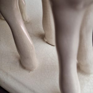 Pode incluir: Escultura de cer&acirc;mica creme com as pernas de um animal, possivelmente um veado ou cavalo. As pernas s&atilde;o lisas e arredondadas, com um acabamento brilhante. A base &eacute; retangular com uma apar&ecirc;ncia rachada e envelhecida.