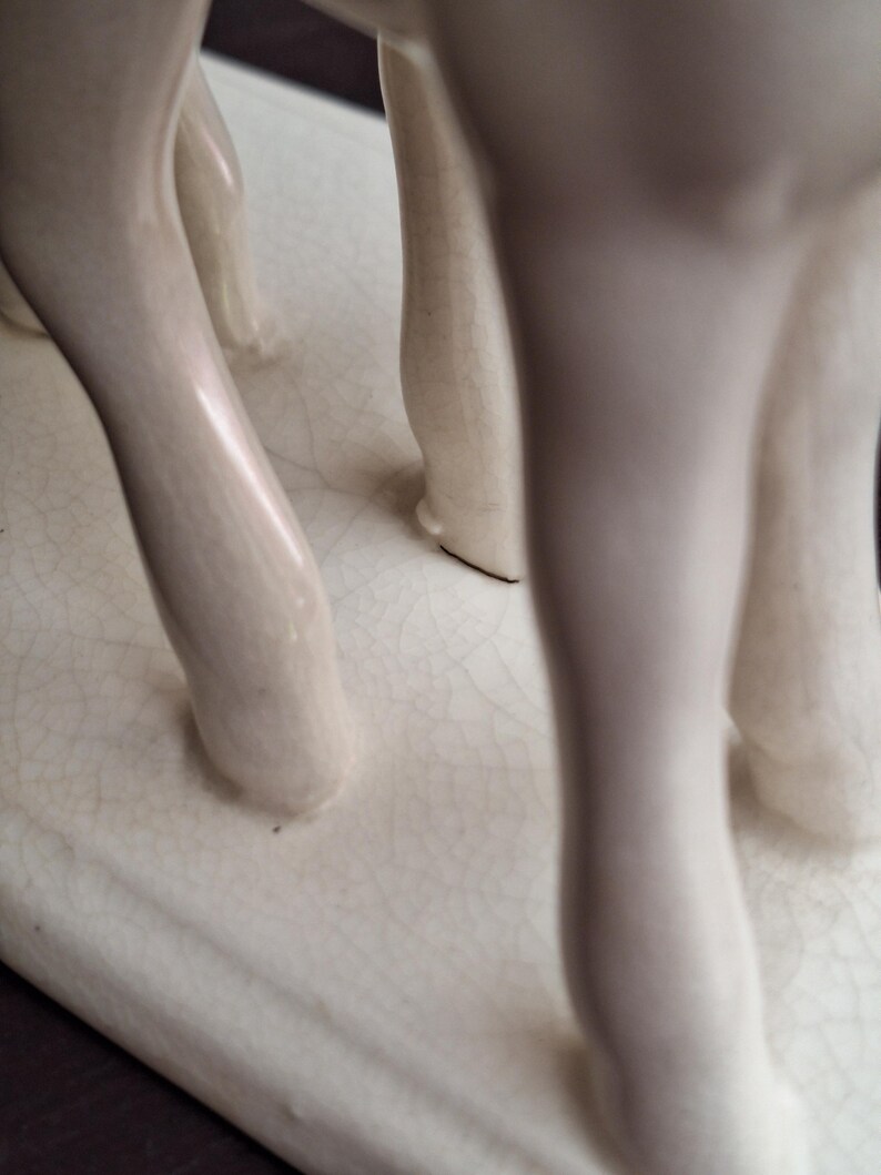Pode incluir: Escultura de cer&acirc;mica creme com as pernas de um animal, possivelmente um veado ou cavalo. As pernas s&atilde;o lisas e arredondadas, com um acabamento brilhante. A base &eacute; retangular com uma apar&ecirc;ncia rachada e envelhecida.