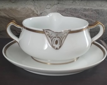 Puede incluir: Salsera de porcelana blanca con borde dorado y diseño floral dorado. La salsera está sobre un plato a juego.