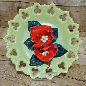 May include: A green ceramic plate with a scalloped edge and cut-out design features two red 3D flowers with green leaves.