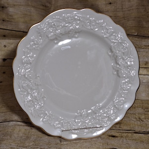 May include: White ceramic dinner plate with a raised floral design and a gold rim.