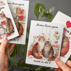 Könnte beinhalten: Vier Grußkarten mit Katzenillustrationen und dem Text "Jesus liebt dich und ich auch" und "Jesus liebt dich". Die Karten zeigen rote Herzen und florale Akzente. Die Katzen sind in verschiedenen Posen dargestellt.