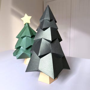 May include: Two paper Christmas trees, one green and one black, with a gold star on top of the green tree. The trees are made of folded paper and have a geometric design.