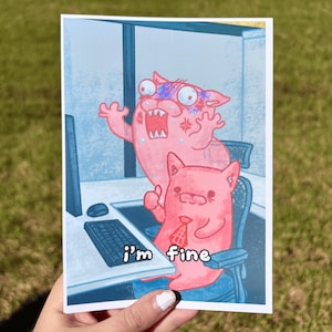 May include: A rectangular print featuring two pink cartoon cats in an office setting. One cat is screaming with wide eyes, while the other sits at a desk wearing a tie, giving a thumbs up with the text i'm fine printed below.