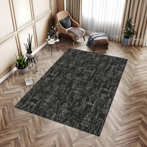 May include: A dark grey rectangular rug featuring a white line drawing pattern of mechanical objects. The rug is placed on a wooden floor with a herringbone pattern. The room has a neutral colour palette with a chair and side table.