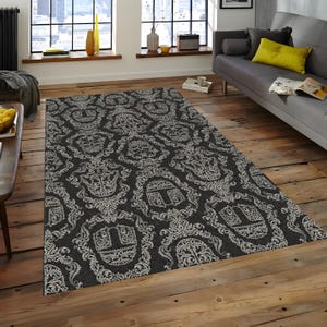 May include: A rectangular rug featuring a repeating pattern of white, crown-like motifs on a dark grey backdrop. The rug is laid on a wooden floor, within a living room setting.