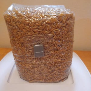 May include: A clear plastic bag filled with brown rice grains. The bag is sealed and has a small gray label on the side.
