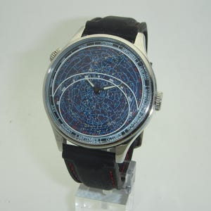 May include: A silver wristwatch with a black leather band. The watch face features a blue background with a star chart and constellations. The watch face also includes month and day markings.