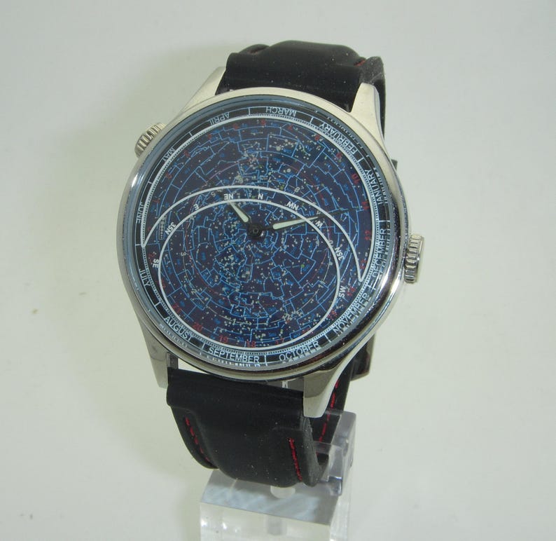 May include: A silver wristwatch with a black leather band. The watch face features a blue background with a star chart and constellations. The watch face also includes month and day markings.