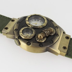 K&ouml;nnte beinhalten: Eine goldfarbene Uhr mit einem mehrschichtigen Zifferblatt und einem gr&uuml;nen Canvas-Armband. Das Zifferblatt der Uhr hat drei runde Zifferbl&auml;tter, eines mit r&ouml;mischen Ziffern und zwei mit arabischen Ziffern. Die Uhr hat einen Steampunk-Look.
