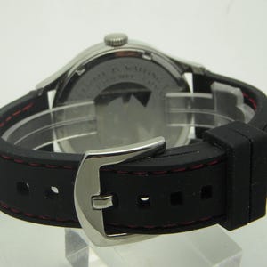 May include: A silver watch with a black rubber strap and red stitching. The watch has a silver buckle and a white dial. The back of the watch is visible, showing the text "Limited Edition" and "Swiss Made".
