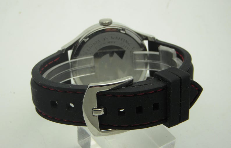 May include: A silver watch with a black rubber strap and red stitching. The watch has a silver buckle and a white dial. The back of the watch is visible, showing the text "Limited Edition" and "Swiss Made".