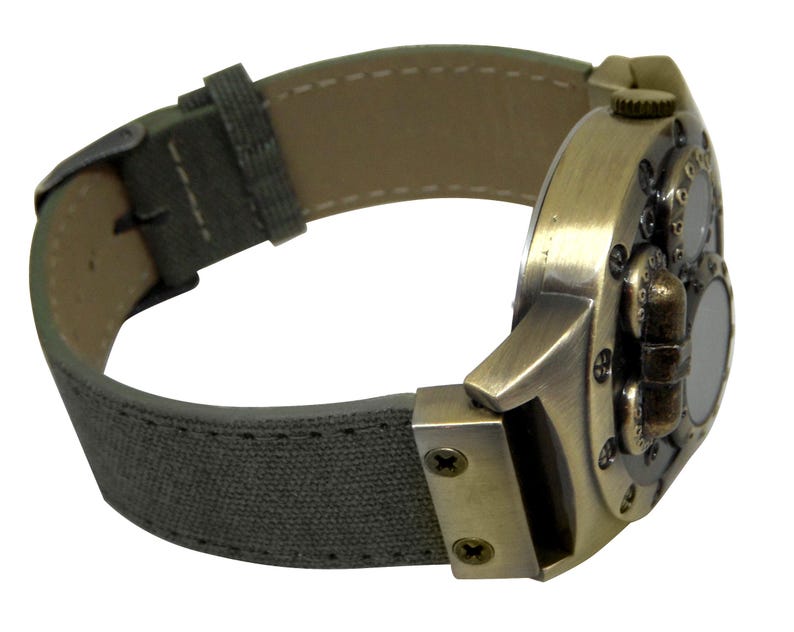 K&ouml;nnte beinhalten: Eine bronzefarbene Uhr mit einem einzigartigen, mehrschichtigen Design. Die Uhr hat ein graues Canvas-Armband mit N&auml;hten.