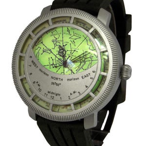 May include: A silver-toned wristwatch with a black rubber band. The watch face features a green star chart with constellations and a compass-like dial with the words "West Horizon", "North 35&deg;50&deg;", "East Horizon", and "Midnight".