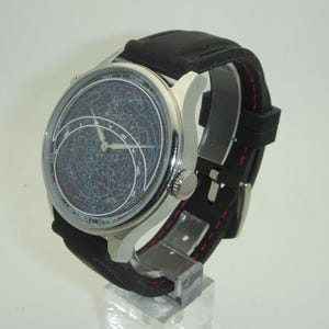 May include: A silver wristwatch with a black leather band and a constellation-themed face. The watch face features a detailed map of the night sky with constellations and stars.
