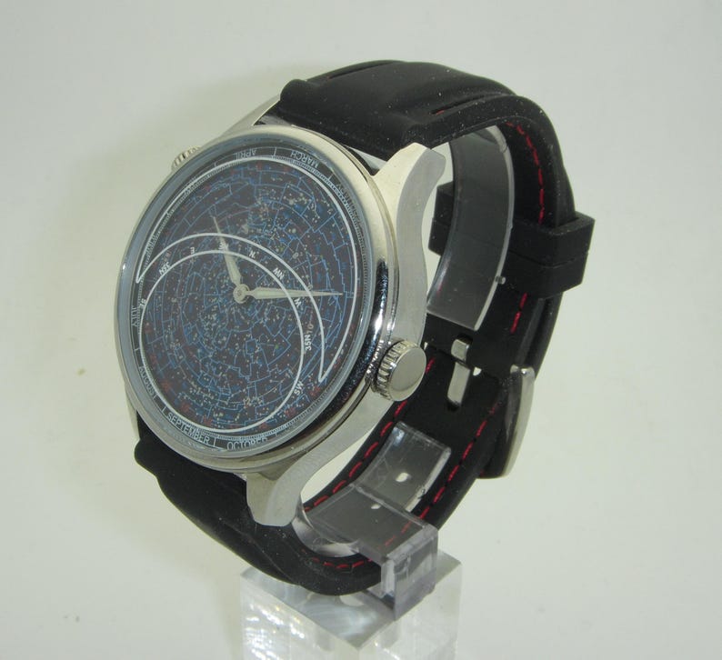 May include: A silver wristwatch with a black leather band and a constellation-themed face. The watch face features a detailed map of the night sky with constellations and stars.