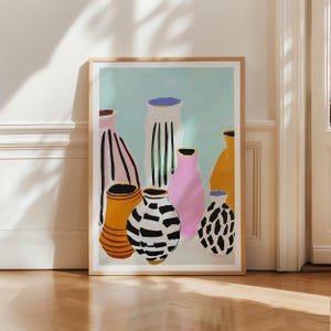 Puede incluir: Una impresión artística enmarcada que presenta una colección de jarrones estilizados en varios colores y patrones. Los jarrones incluyen rayas, manchas y colores sólidos como rosa, amarillo y negro, sobre un fondo azul claro. La obra de arte está en un marco de madera.