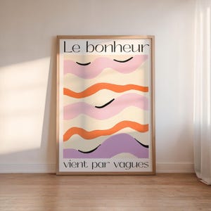 Puede incluir: Impresión artística enmarcada con el texto "Le bonheur vient par vagues". La obra presenta líneas onduladas abstractas en tonos rosa, naranja y morado sobre un fondo crema. La impresión está encerrada en un marco de madera marrón claro.