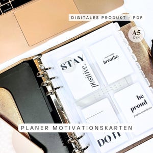 Può includere: Un raccoglitore A5 color oro con schede motivazionali. Le schede presentano frasi come "Stay Positive" e "Breathe". Il raccoglitore è aperto, rivelando le schede e un interno nero. I testi "DIGITALES PRODUKT - PDF" e "PLANER MOTIVATIONSKARTEN" sono visibili.
