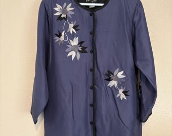 May include: A periwinkle blue jacket with long sleeves and a round neckline. The jacket features a black trim and is adorned with embroidered floral designs in shades of white, gray, and black. The jacket has a button-up front.