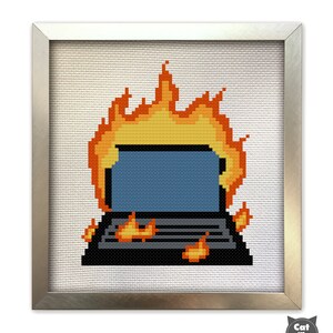 May include: A framed cross-stitch design of a computer on fire. The computer is black with a blue screen and a keyboard. The flames are orange and yellow.