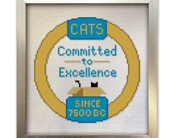May include: Cross-stitch artwork in a silver frame. The design features a gold ring with the text "CATS Committed to Excellence" in blue. A cat peeks out of a box. The text "SINCE 7500 BC" is below the box.