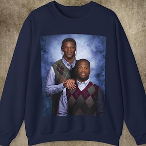 May include: A navy blue sweatshirt featuring a photograph of two people wearing sweaters. The image is printed on the front of the sweatshirt.