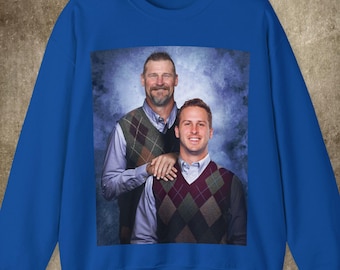 May include: A royal blue sweatshirt with a photo of two people wearing patterned sweaters. The photo shows two people smiling and standing next to each other. The person on the left is wearing a green and brown patterned sweater and the person on the right is wearing a red and white patterned sweater.